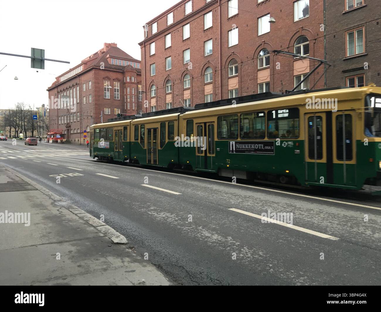 I tram si spostano attraverso le strade della città di Helsinki, mostrando le classiche carrozze verdi, le rotaie, i cavi sospesi e i dintorni urbani Foto Stock