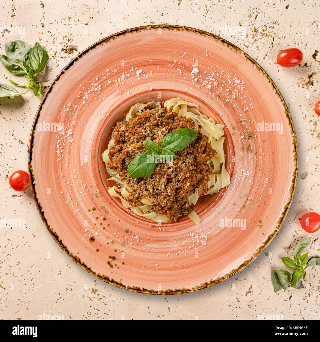 Deliziose tagliatelle con salsa alla bolognese, parmigiano e basilico su un elegante piatto rosa Foto Stock