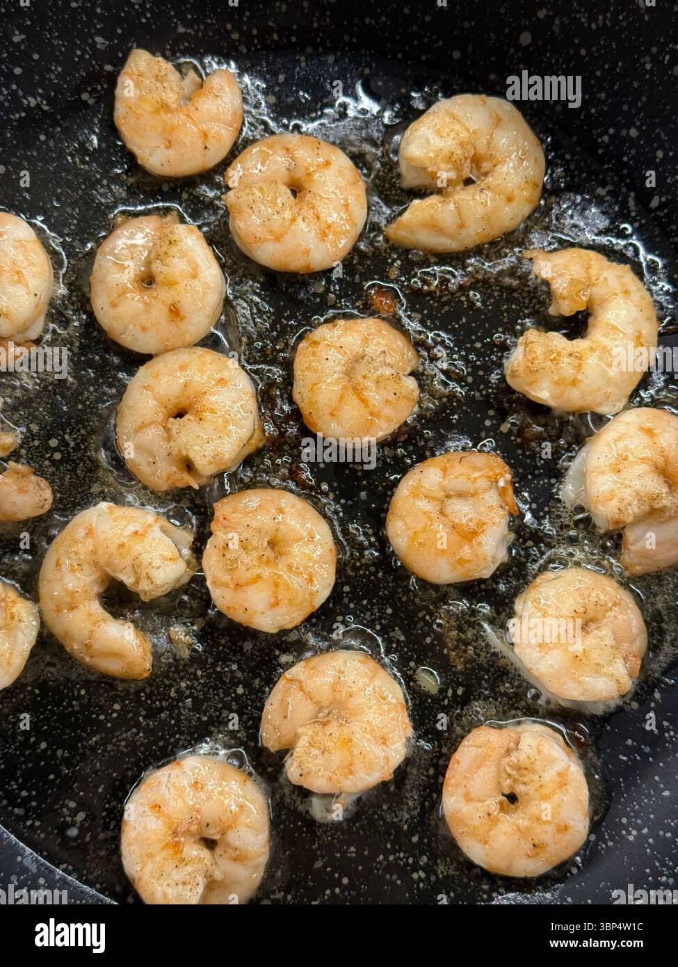L'immagine mostra la frittura di gamberi sbucciati nell'olio in una padella nera antiaderente. I gamberi sono parzialmente cotti e presentano una cucitura marrone-arancio chiaro, indicata Foto Stock