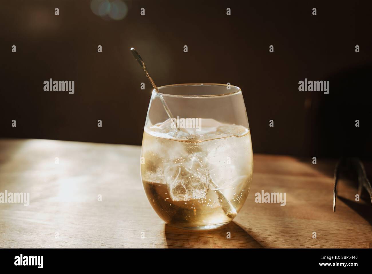 Sake fresco servito su ghiaccio in vetro illuminato dal sole su legno, ambiente elegante e semplice, ideale per cene di lusso o blog di stile, ospitalità e cocktail bar Foto Stock