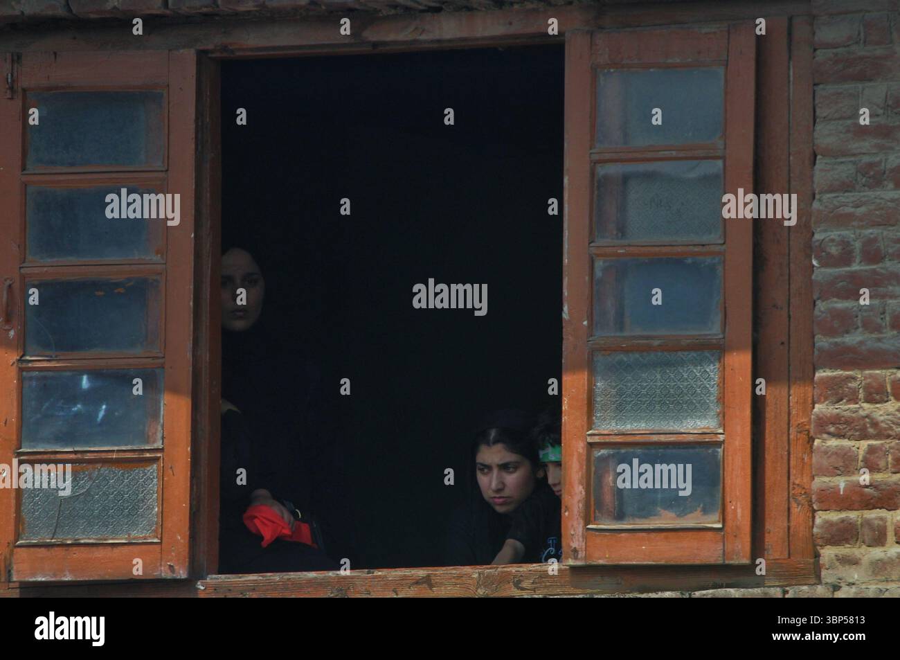 Le donne kashmiri guardano da una finestra mentre una processione di Muharram passa attraverso una strada a Srinagar il 6 luglio 2025, segnando il decimo giorno delle commemorazioni di Ashura. Foto Stock