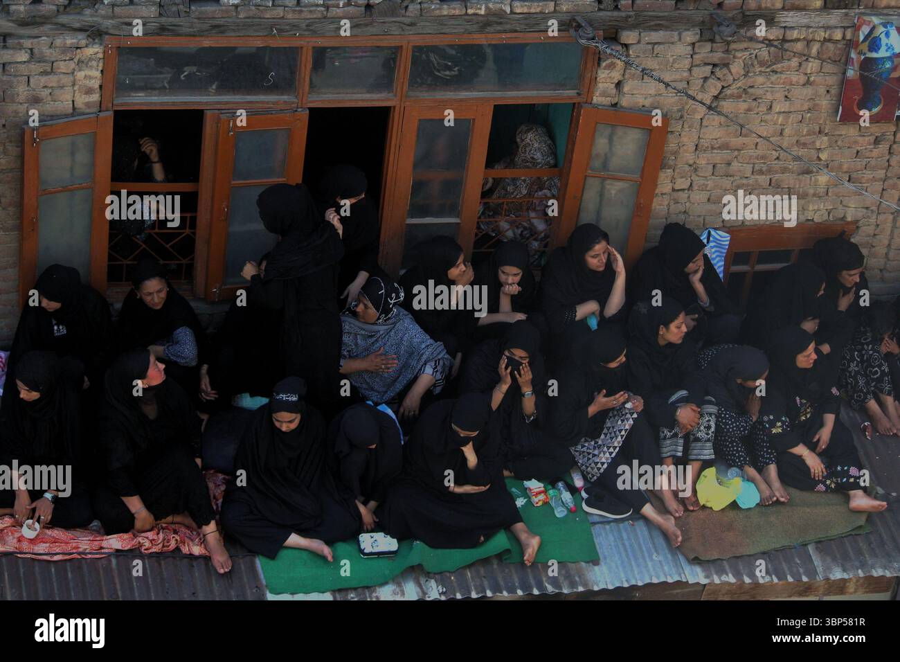 Le donne musulmane sciite kashmiri si siedono su un tetto per guardare la decima processione Muharram a Srinagar il 6 luglio 2025, mentre i lutti commemorano il martirio dell'Imam Hussain durante l'annuale osservanza Ashura. Foto Stock