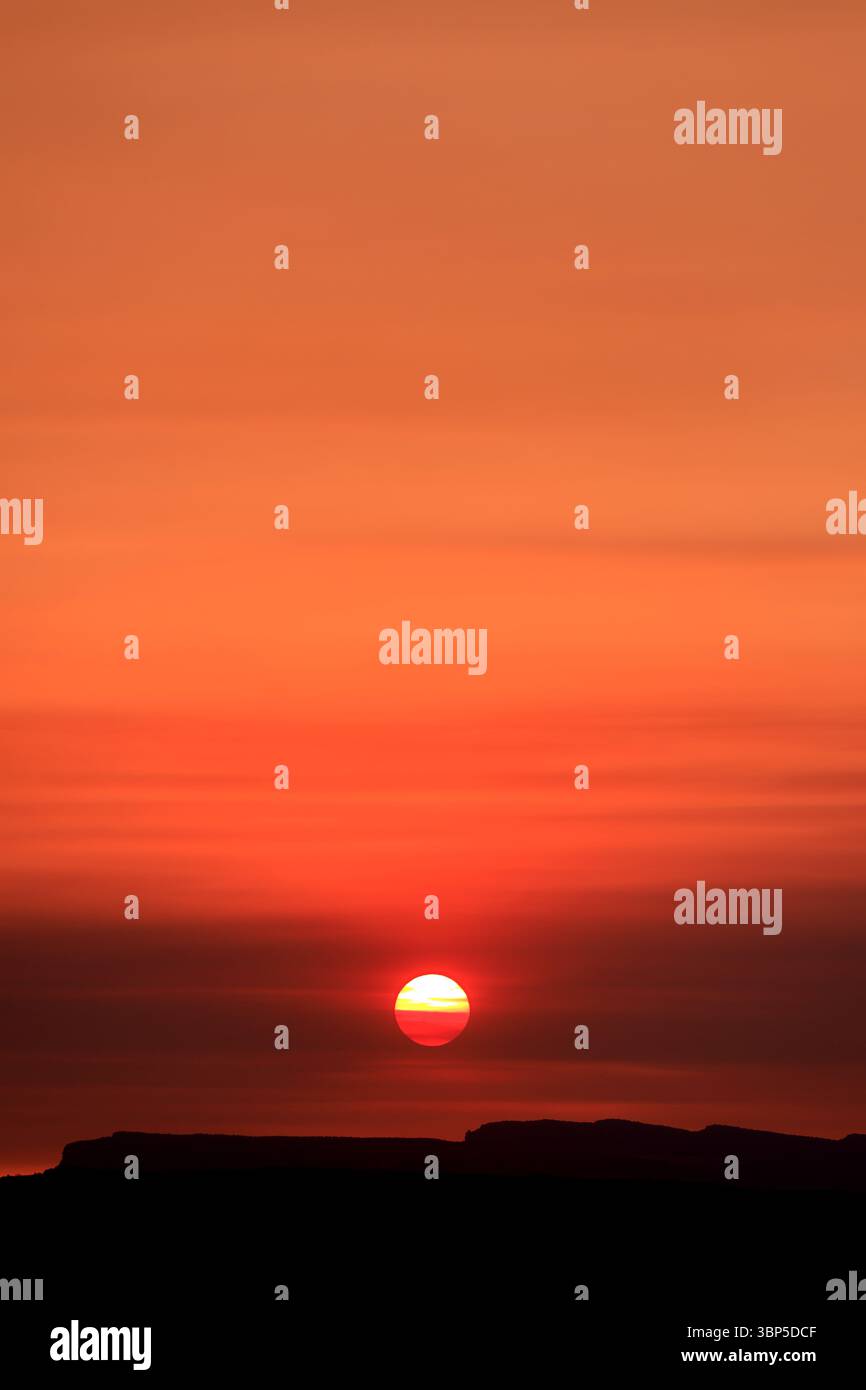 Il sole affonda lentamente dietro le mesas lontane, diffondendo una calda luce arancione attraverso la morbida foschia del deserto in una pausa fugace e perfetta tra il giorno e la notte. Foto Stock