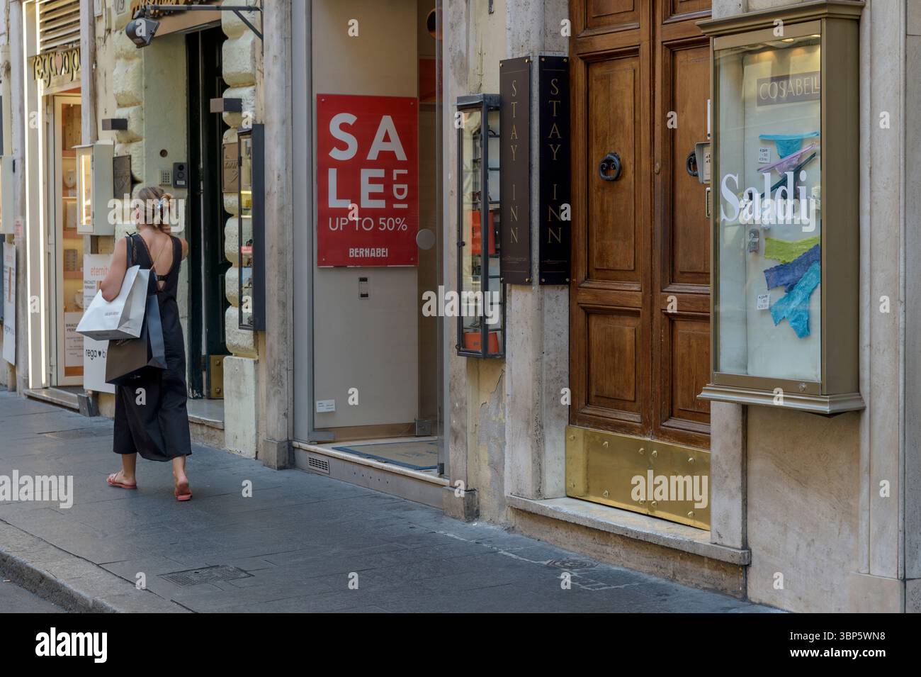 6 luglio 2025, Roma, Italia: Una donna trasporta borse contenenti prodotti acquistati in una delle vie dello shopping i cui negozi espongono le parole vendite nelle loro vetrine durante il periodo estivo di vendita a Roma. I saldi estivi sono iniziati il 5 luglio in tutta Italia, ad eccezione della provincia autonoma di Bolzano, dove inizieranno il 16 luglio.secondo le stime dell'Ufficio ricerche Confcommercio, quest'anno ogni famiglia spenderà in media 203 euro in abbigliamento scontato, pari a 92 euro pro capite, per un valore complessivo di 3,3 miliardi di euro. (Immagine di credito: © Marcello Valeri/ZUMA Foto Stock