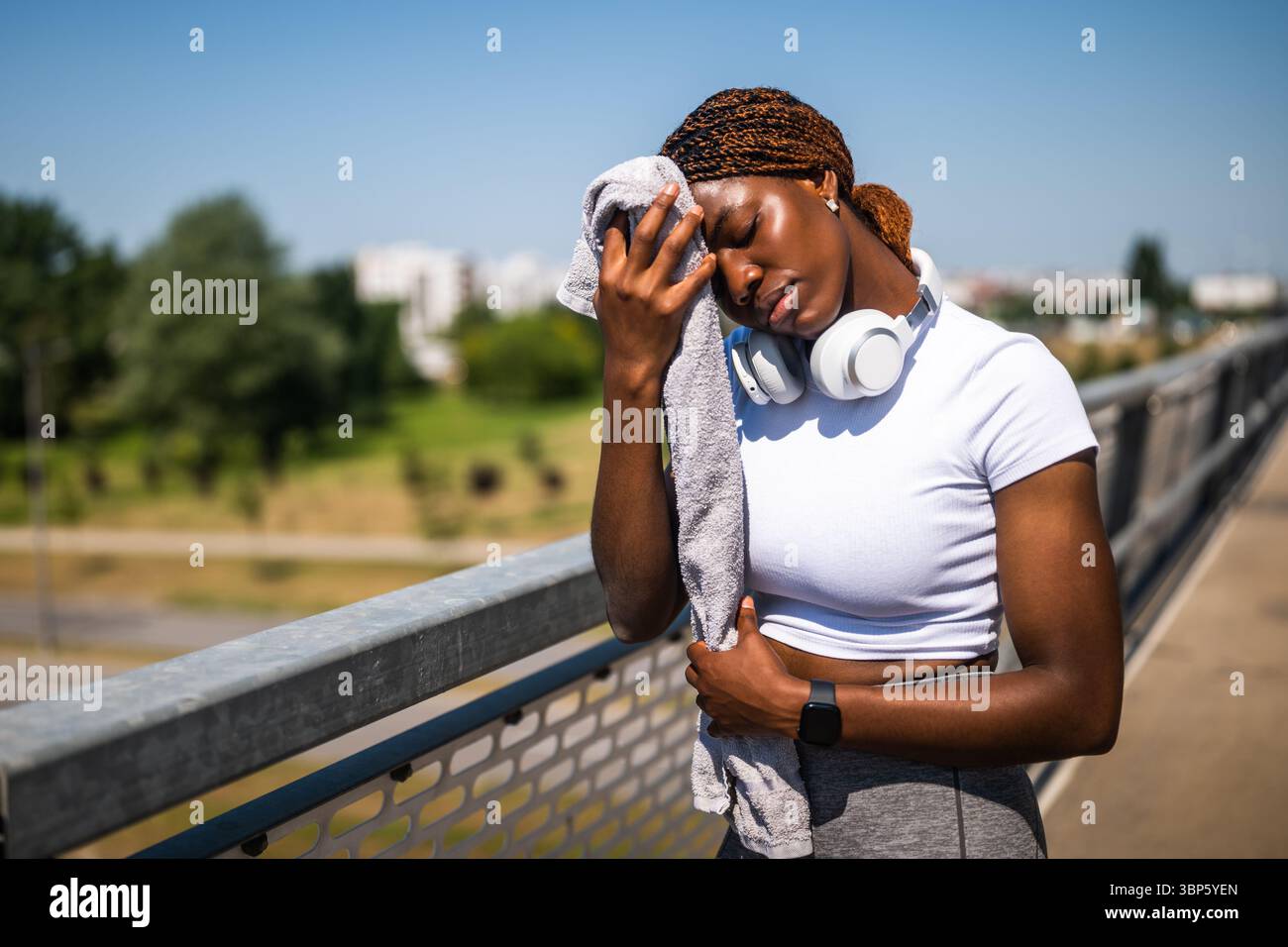 Donna afro-americana che sembra delusa e preoccupata mentre si pulisce sudore dal viso con un asciugamano dopo un intenso esercizio fisico sul ponte cittadino. Foto Stock