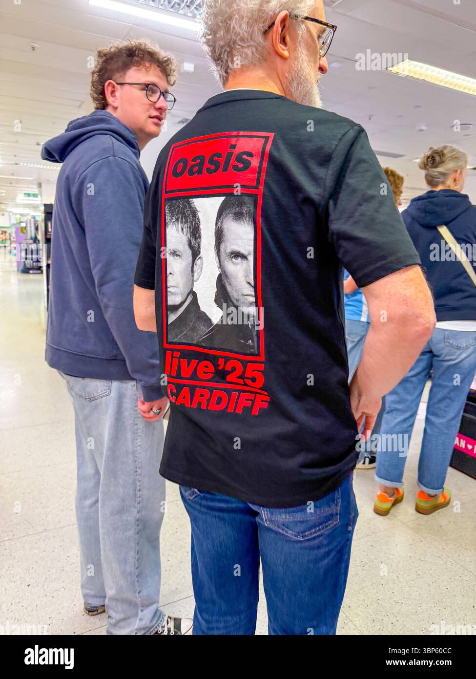 Oasis Tour Cardiff i fan dei concerti indossano magliette e articoli di merchandising fuori Venu - Immagine stock catturata con smartphone