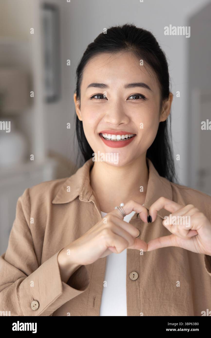 Donna che mostra di fare gesti a forma di cuore con le dita Foto Stock