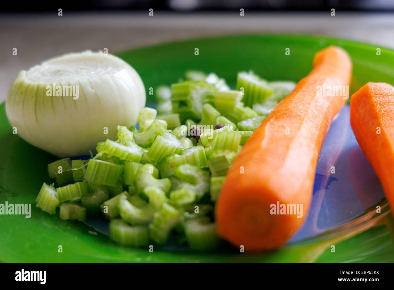 Il piatto verde mostra verdure fresche, tra cui mezza cipolla sbucciata, gambi di sedano tritati e due carote intere. Foto Stock