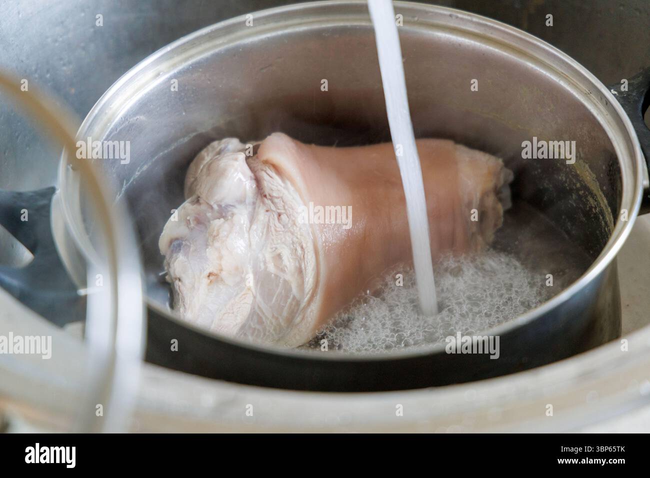Un pezzo di carne viene lavato o bollito in una pentola piena d'acqua, con un getto d'acqua che scorre dall'alto. Foto Stock