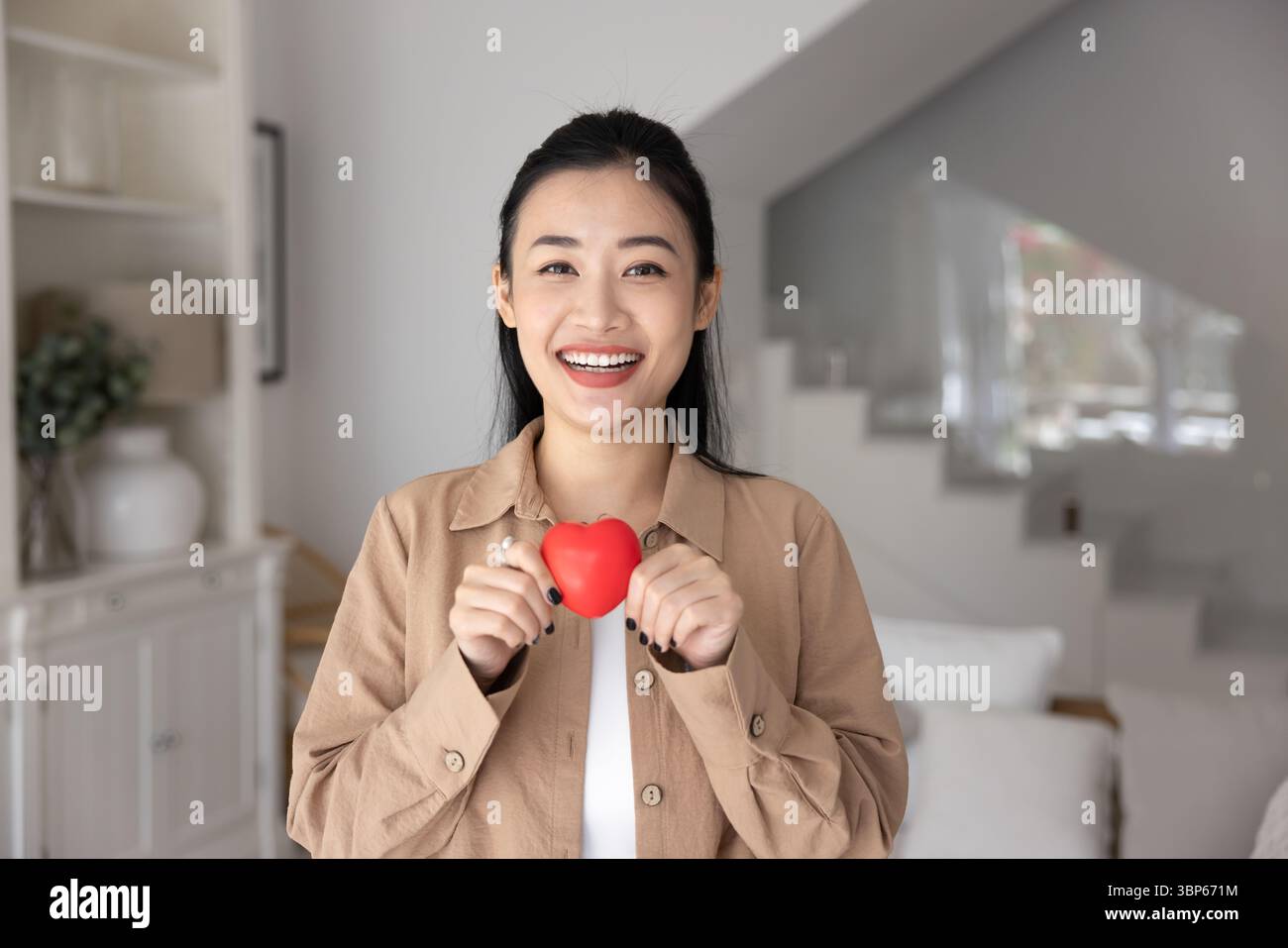 Donna asiatica che tiene in mano una piccola forma di cuore rossa Foto Stock