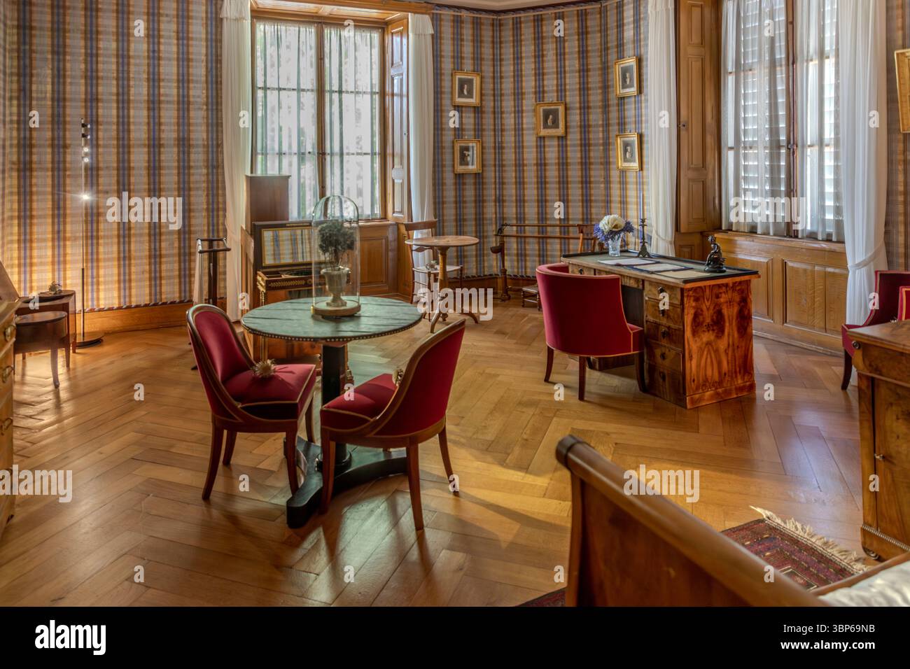 Elegante sala storica nel castello di Arenenberg a Salenstein, Thurgau, Svizzera. La camera, possibilmente un salotto o uno studio, è arredata con mobili antichi, carta da parati a motivi geometrici e pavimento in parquet a spina di pesce. Fornisce un'idea della vita di ex residenti come la regina Ortensia e Napoleone III Foto Stock