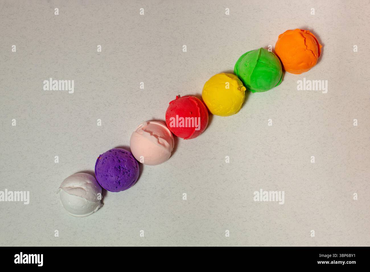 Palline da gelato multicolore in fila su sfondo grigio. Colori vivaci Foto Stock