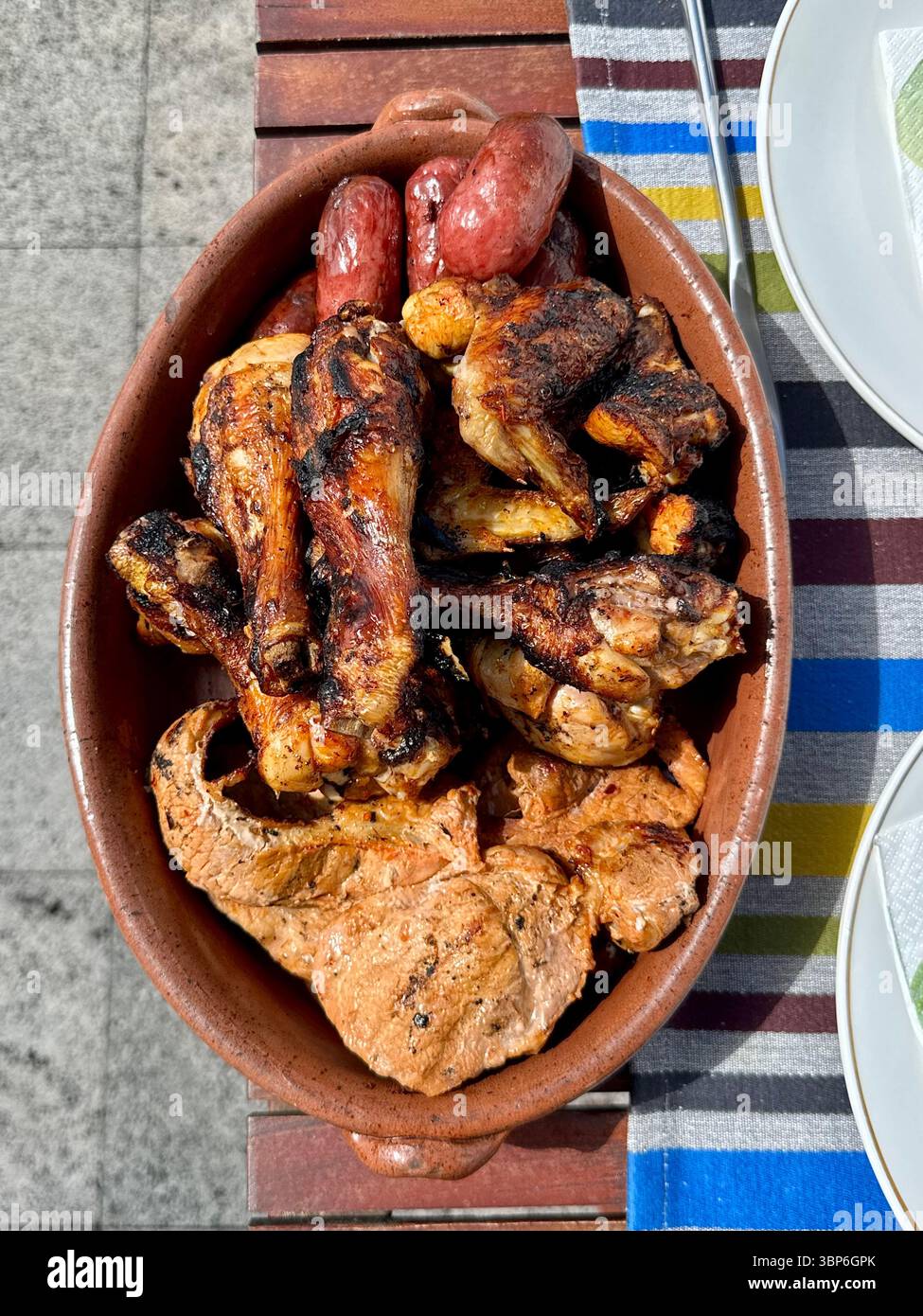 Piatto misto di carne alla griglia servito in un piatto di terracotta, con ali di pollo, costolette di maiale e salsicce. - Immagine stock catturata con smartphone