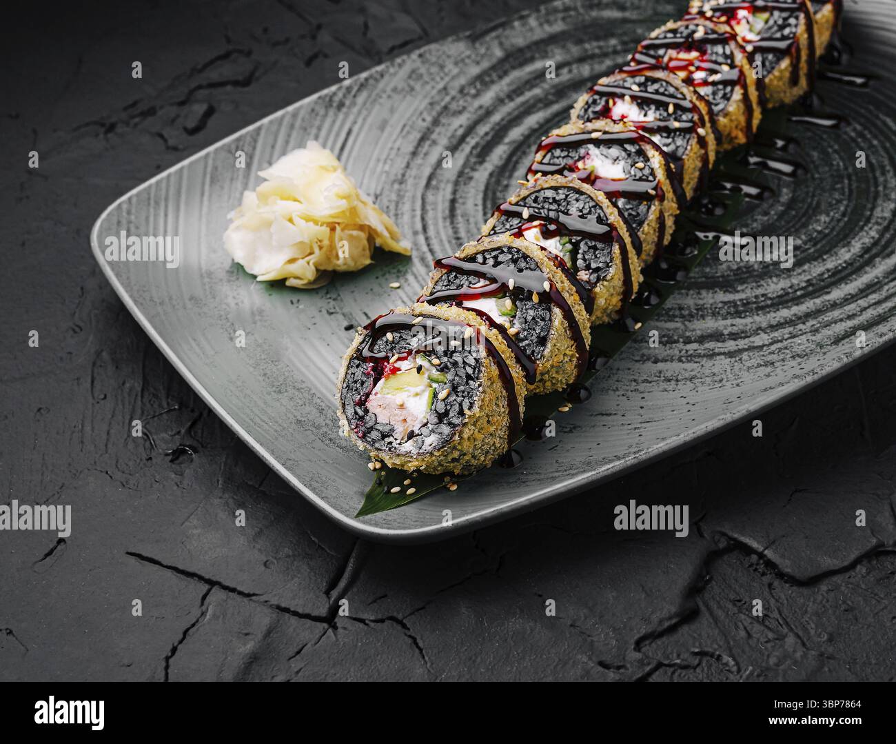 Cibo, Uno splendido sushi roll è presentato su un elegante piatto grigio, caratterizzato da uno strato esterno croccante e condimenti vivaci. Accompagnato da zenzero sottaceto, Th Foto Stock