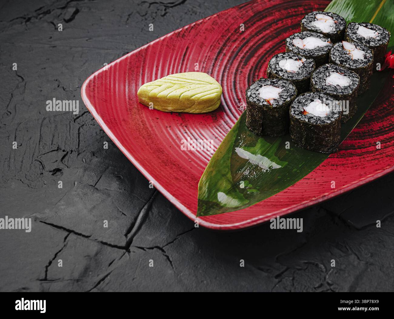 Cibo, deliziosi sushi roll disposti ordinatamente su un piatto rosso con una foglia verde e una piccola dose di wasabi. L'ambientazione mette in risalto l'elegante presentazione Foto Stock