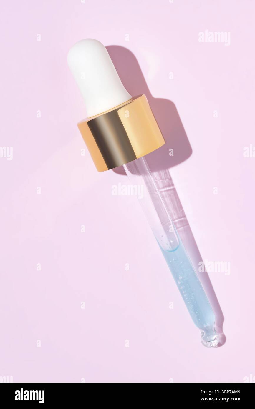 Primo piano della pipetta con il versamento di siero liquido e ombre su sfondo rosa. Cosmetici alla moda con ombre dure Foto Stock