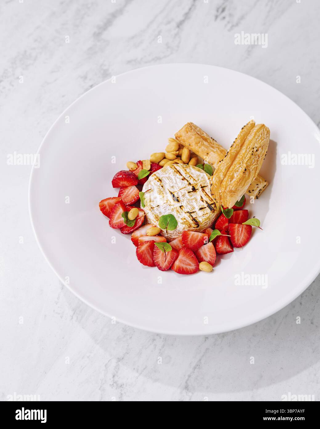 Cibo, squisito ed elegante presentazione di formaggi barbecue gourmet con pasta sfoglia dolce placcata e fragole fresche su un piatto bianco. In mostra con un top Foto Stock