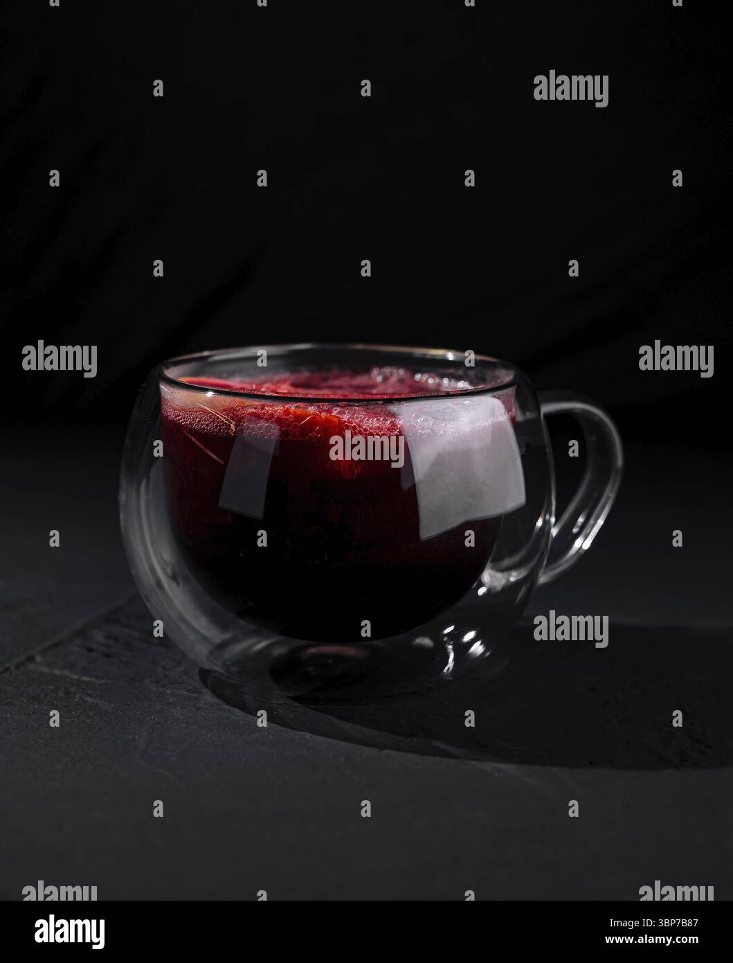 Cibo, Una moderna tazza di vetro a doppia parete piena di tè rosso, isolata su uno sfondo scuro e umido Foto Stock