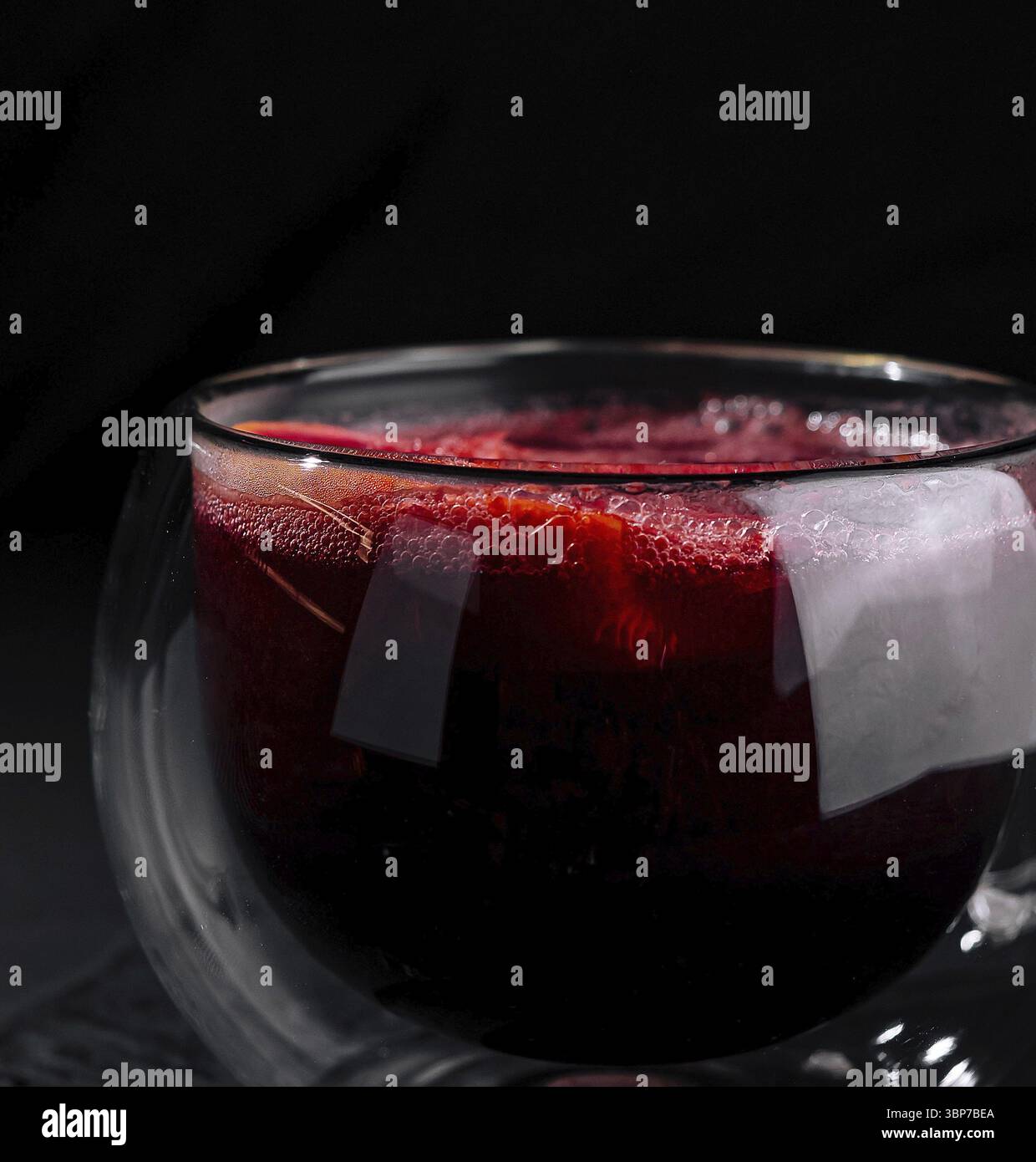Cibo, Una moderna tazza di vetro a doppia parete piena di tè rosso, isolata su uno sfondo scuro e umido Foto Stock
