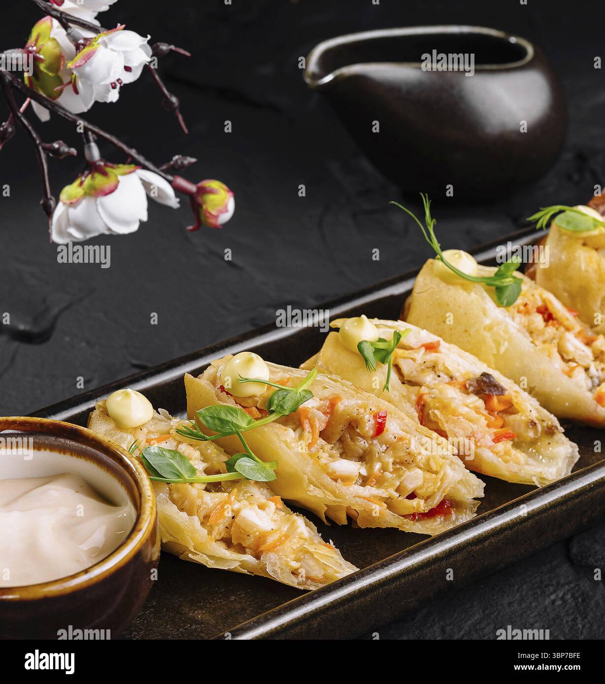Cibo, piatto di deliziosi gnocchi al vapore serviti con salsa accanto a un ramo fiorito Foto Stock