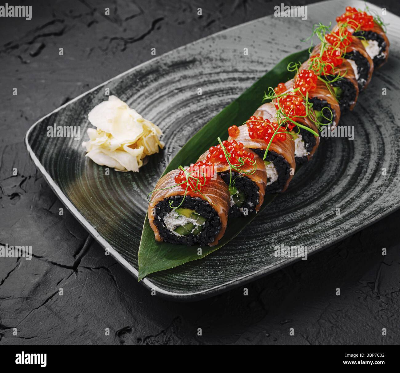 Il cibo, i sushi roll appena fatti sono disposti elegantemente su un piatto scuro. Condito con uova vivaci e guarnito con cipolle verdi, il piatto è accompagnatore Foto Stock