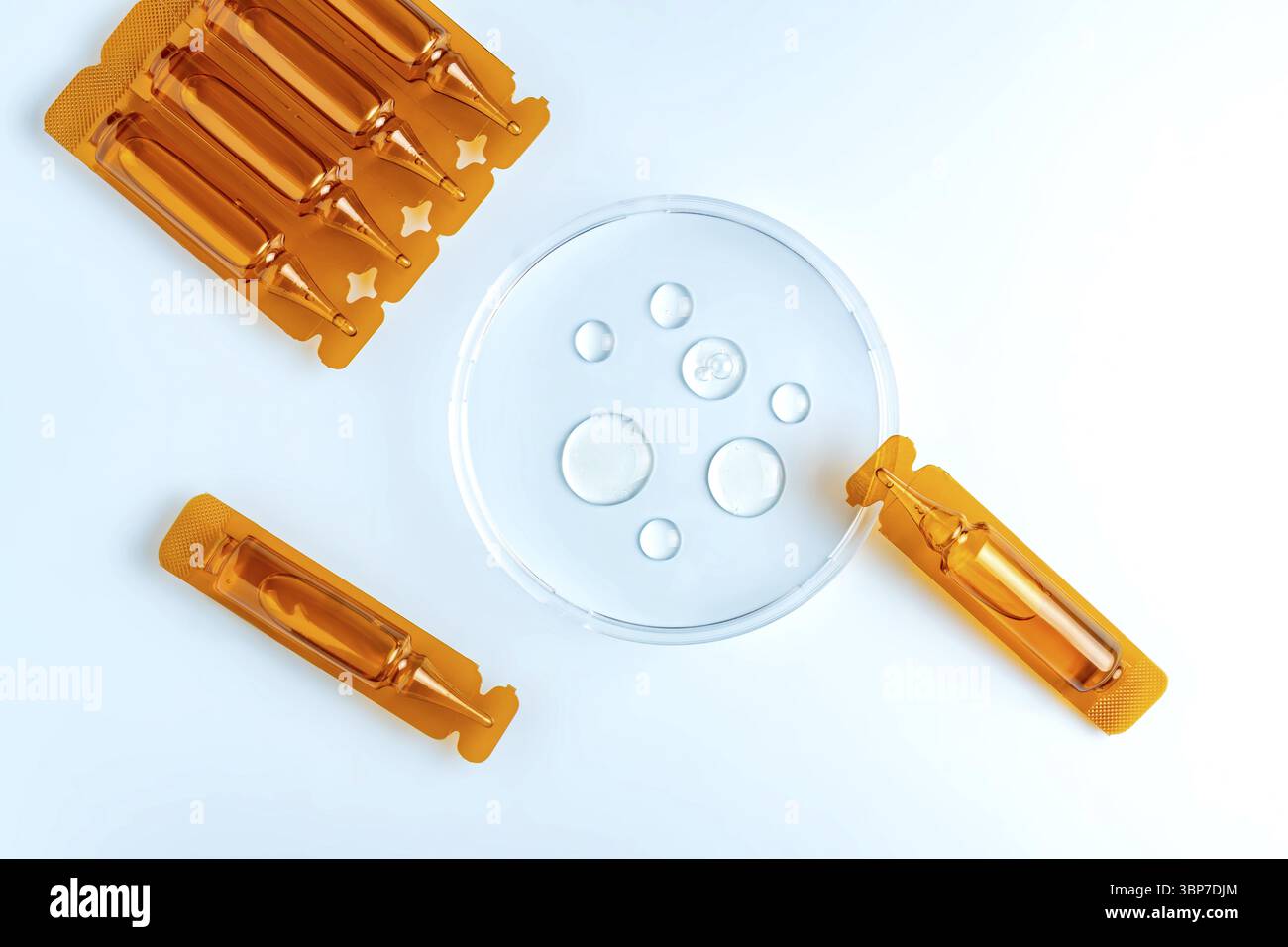 Un olio o siero per la cura dei capelli in ampili o capsule di plastica marrone su sfondo blu con campioni di olio in capsula di Petri, mockup di commercializzazione del prodotto Foto Stock