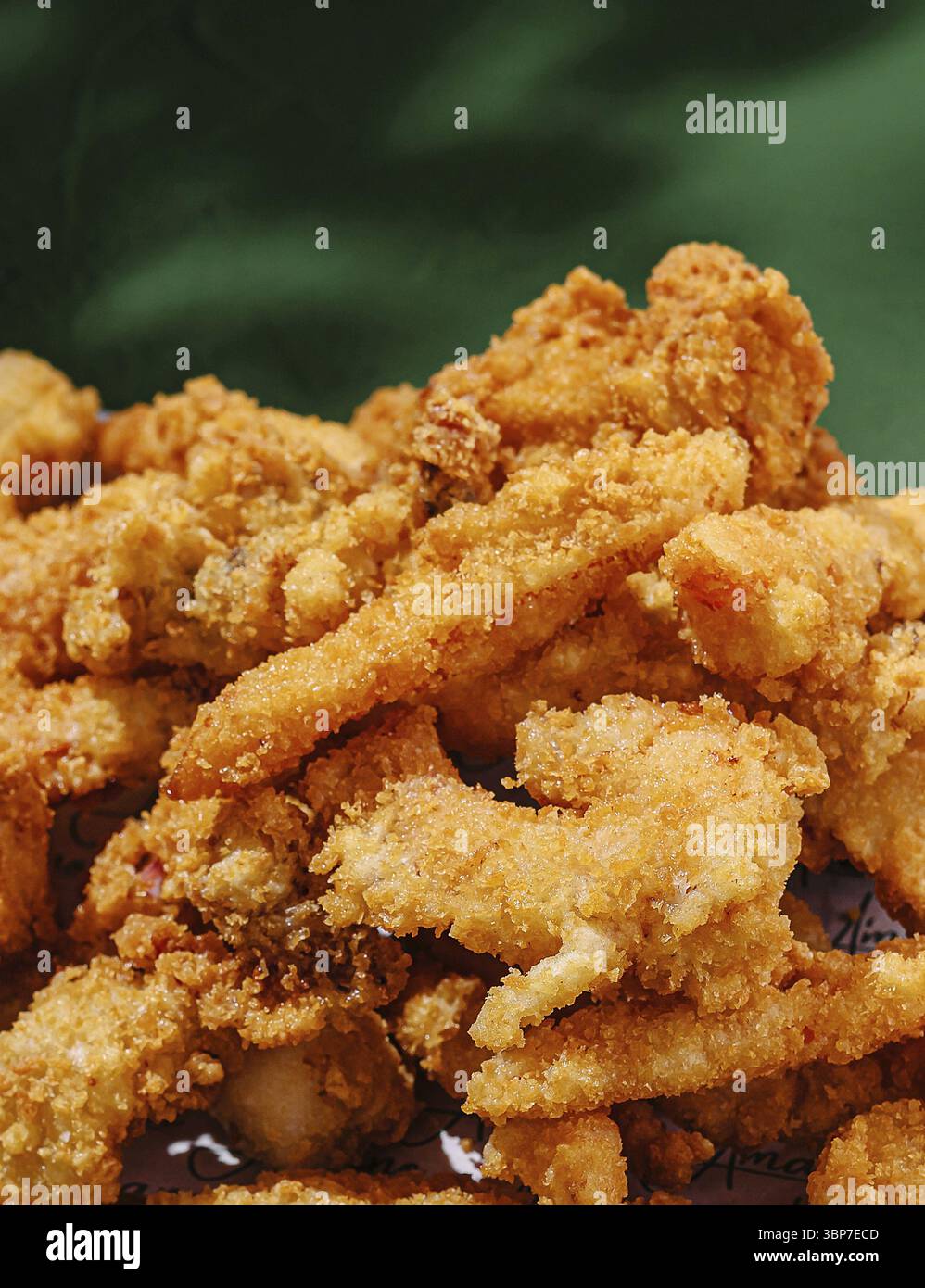 Cibo, Una generosa porzione di pollo fritto dorato e croccante si trova su una superficie a motivi geometrici. Lo sfondo presenta un colore verde brillante che migliora Foto Stock