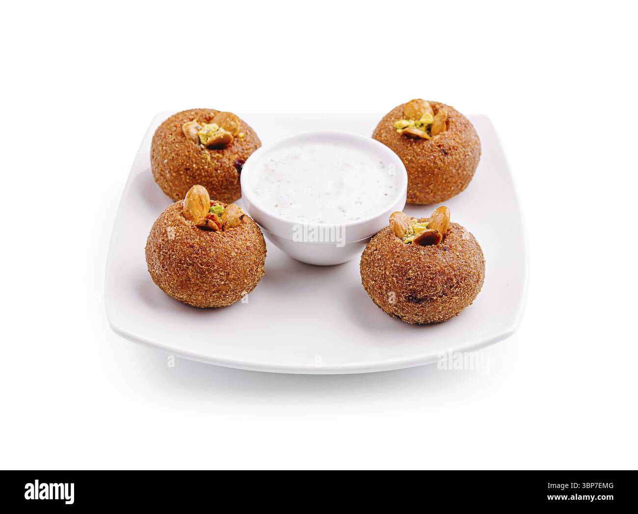 Cibo, quattro spuntini rotondi dorati sono disposti su un piatto bianco, ciascuno ricoperto di noci. Una piccola ciotola di salsa cremosa completa il piatto, Foto Stock