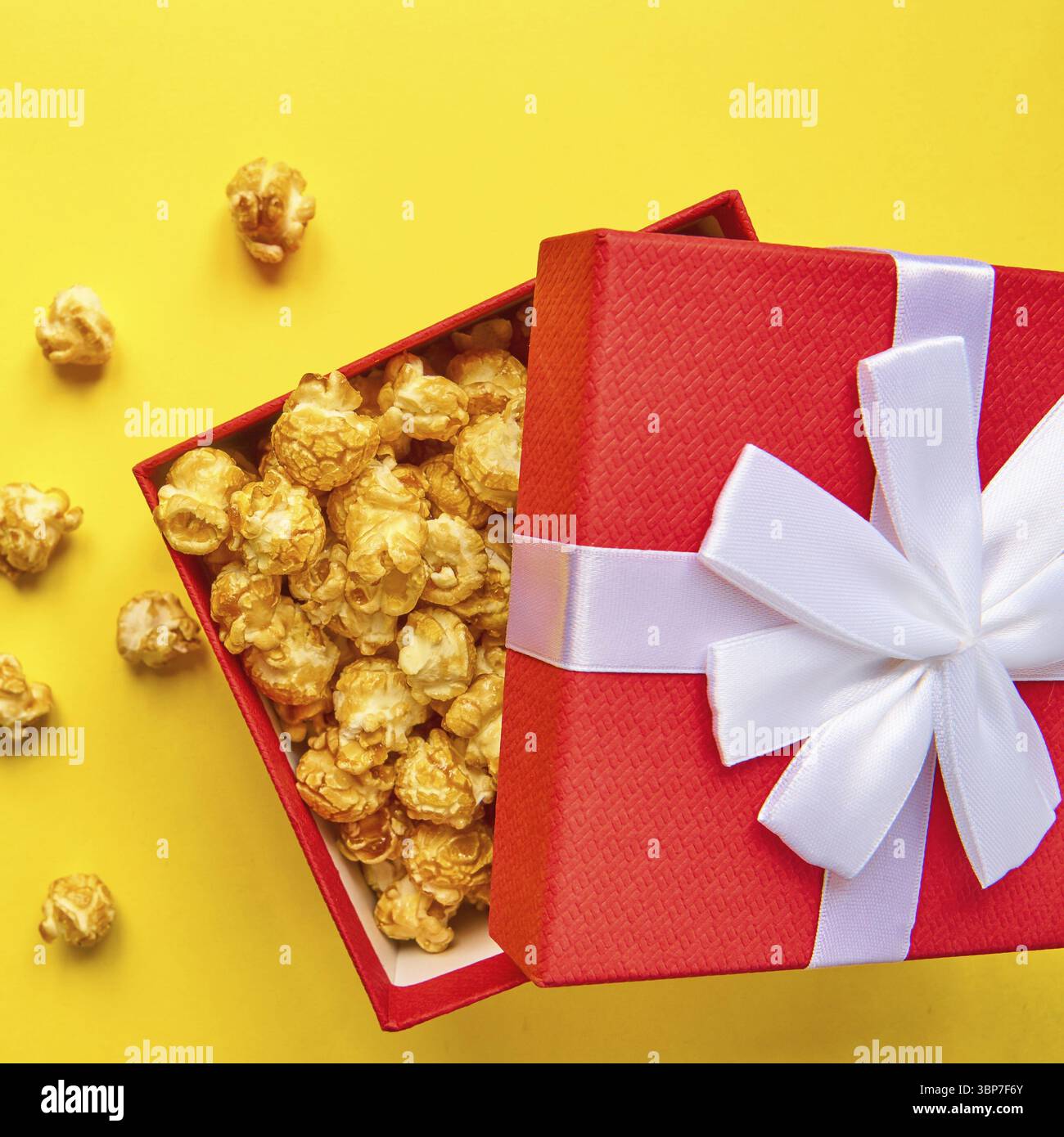 Confezione regalo rossa con fiocco bianco pieno di gustose popcorn al caramello su sfondo giallo Foto Stock