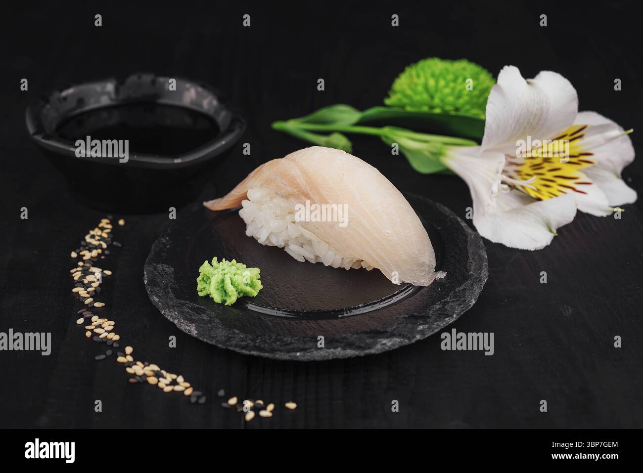 Cibo: Sushi nigiri singolo con pesce bianco servito su un piatto di pietra nera con wasabi, salsa di soia e fiori Foto Stock
