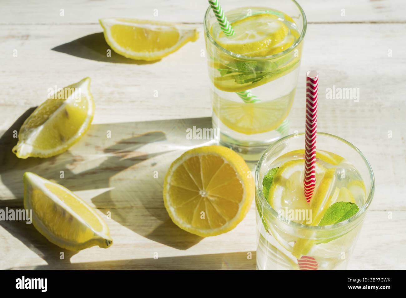 Bicchiere di limonata fatta in casa con limoni, menta e cannucce di carta su fondo rustico in legno. Bevanda rinfrescante estiva. ombre dure Foto Stock