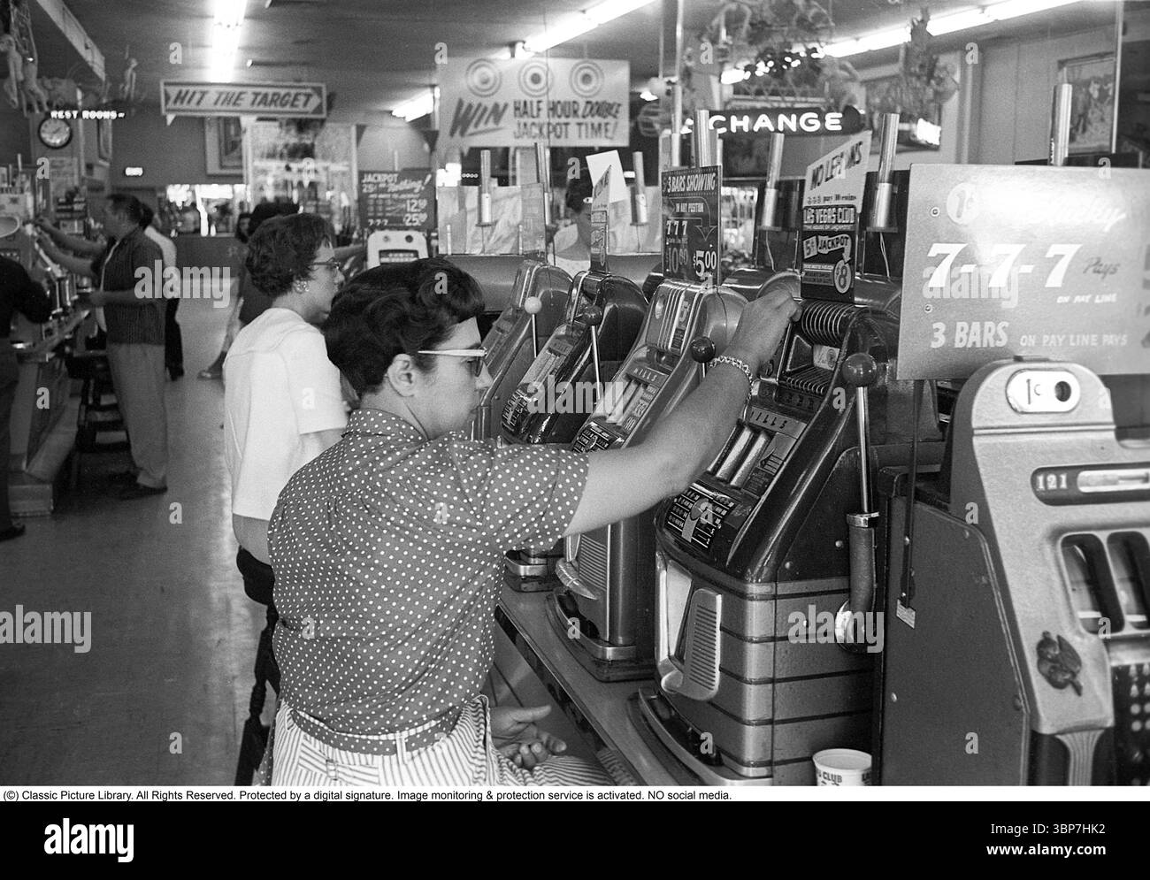 Presso le slot machine negli Stati Uniti 1959. Persone ritratte nelle slot machine. Una macchina da gioco in cui metti una moneta e tiri una leva che inizia a girare tre ruote. Una volta che si fermano e il set di ruote mostra lo stesso simbolo, vinci. Roland Palm rif DV11 Foto Stock