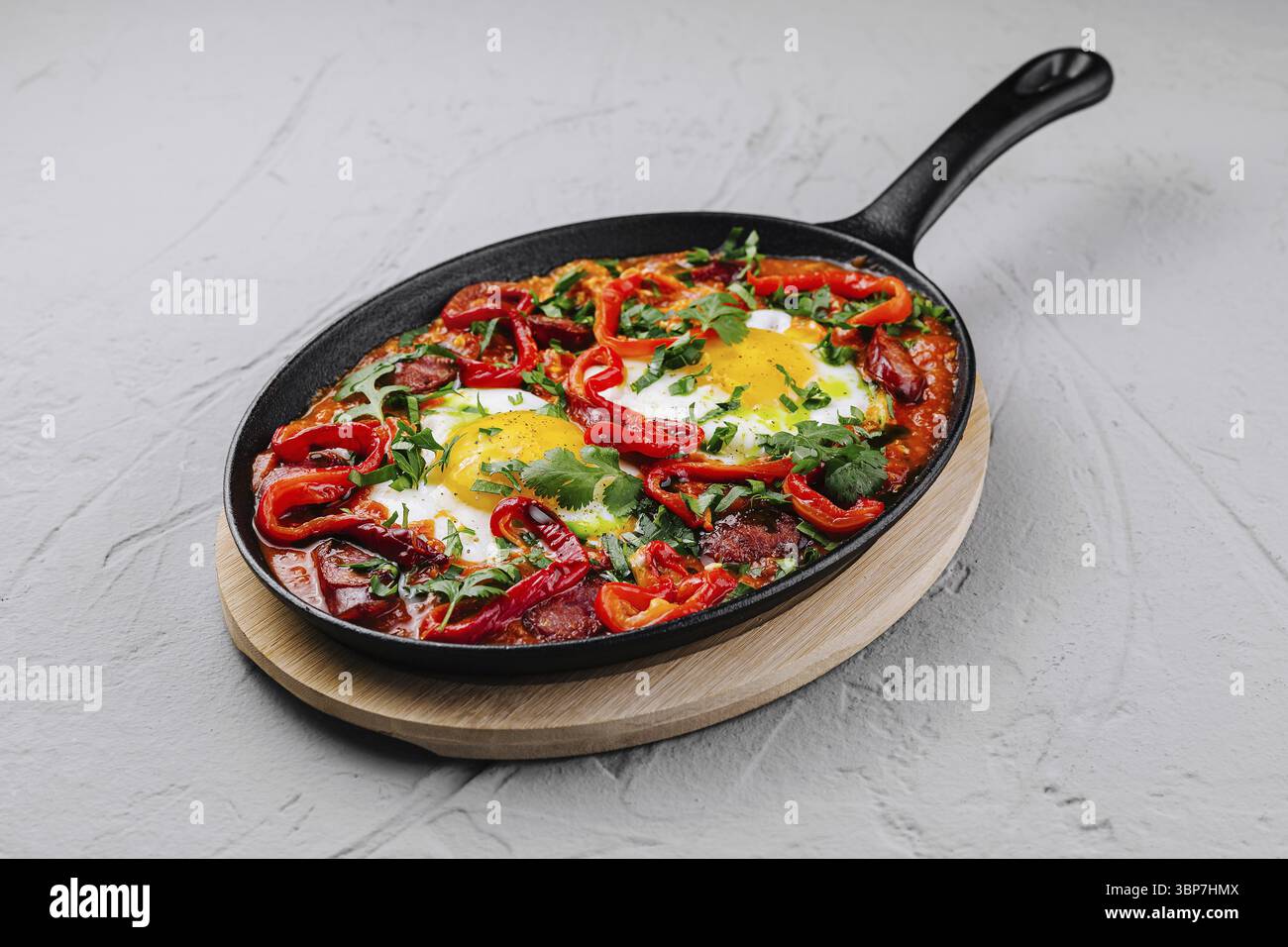 Cibo, shakshuka tradizionale con uova, pomodori e peperoni guarniti con prezzemolo, servito in una padella di ghisa Foto Stock