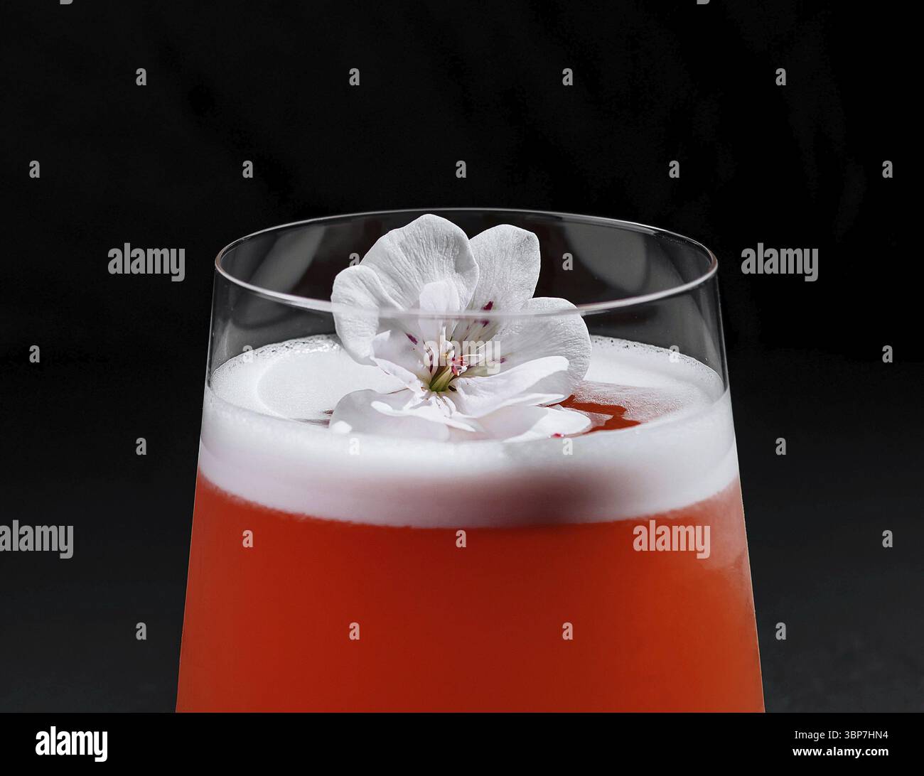 Cibo, cocktail sofisticato adornato da una decorazione floreale bianca su uno sfondo scuro Foto Stock