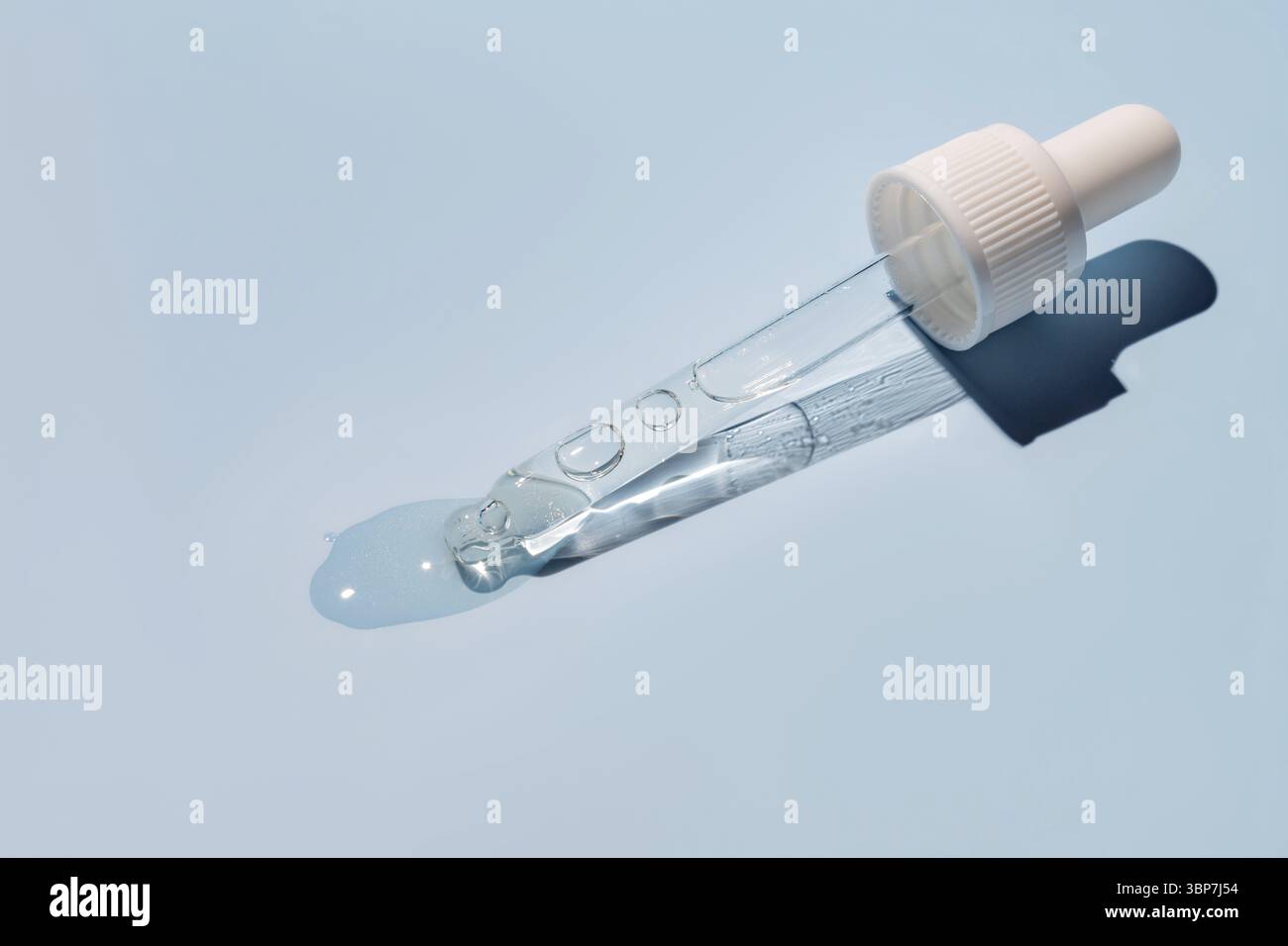 Primo piano della pipetta con il versamento di siero liquido e ombre su sfondo blu. Cosmetici alla moda con ombre dure Foto Stock
