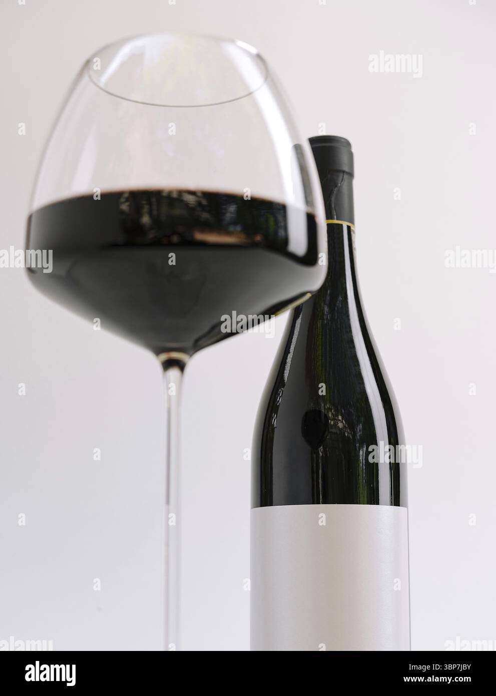 Cibo, Un bicchiere di vino rosso dalla forma splendida è pieno di vino scuro ricco, posizionato accanto a un'elegante bottiglia di vino. Lo sfondo è semplice e non cl Foto Stock
