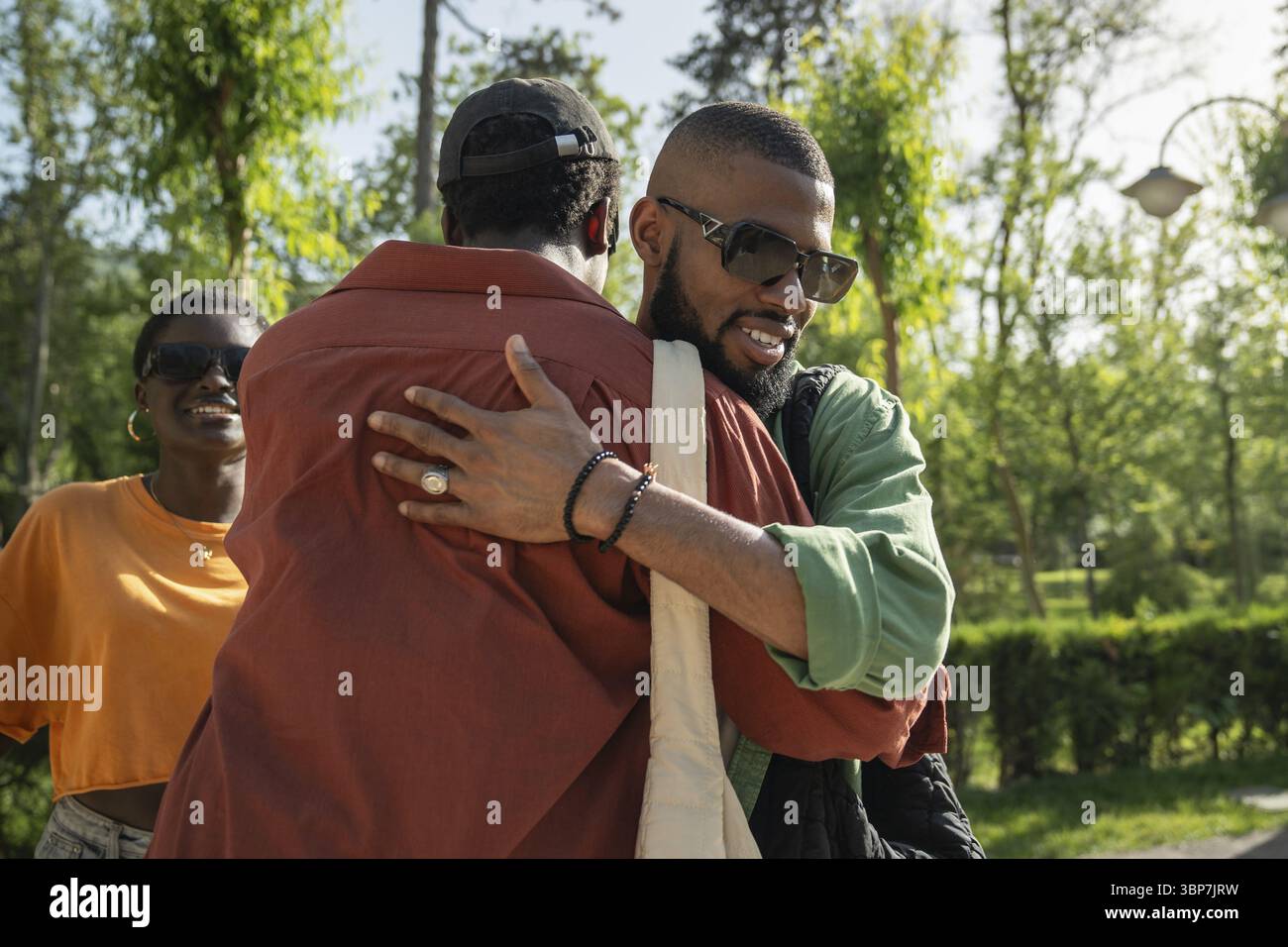Amici neri felici studenti maschi che abbracciano addio. Gli uomini sorridenti saluti, salutano con abbraccio, si sono incontrati per camminare insieme. Gruppo di satis afroamericani Foto Stock