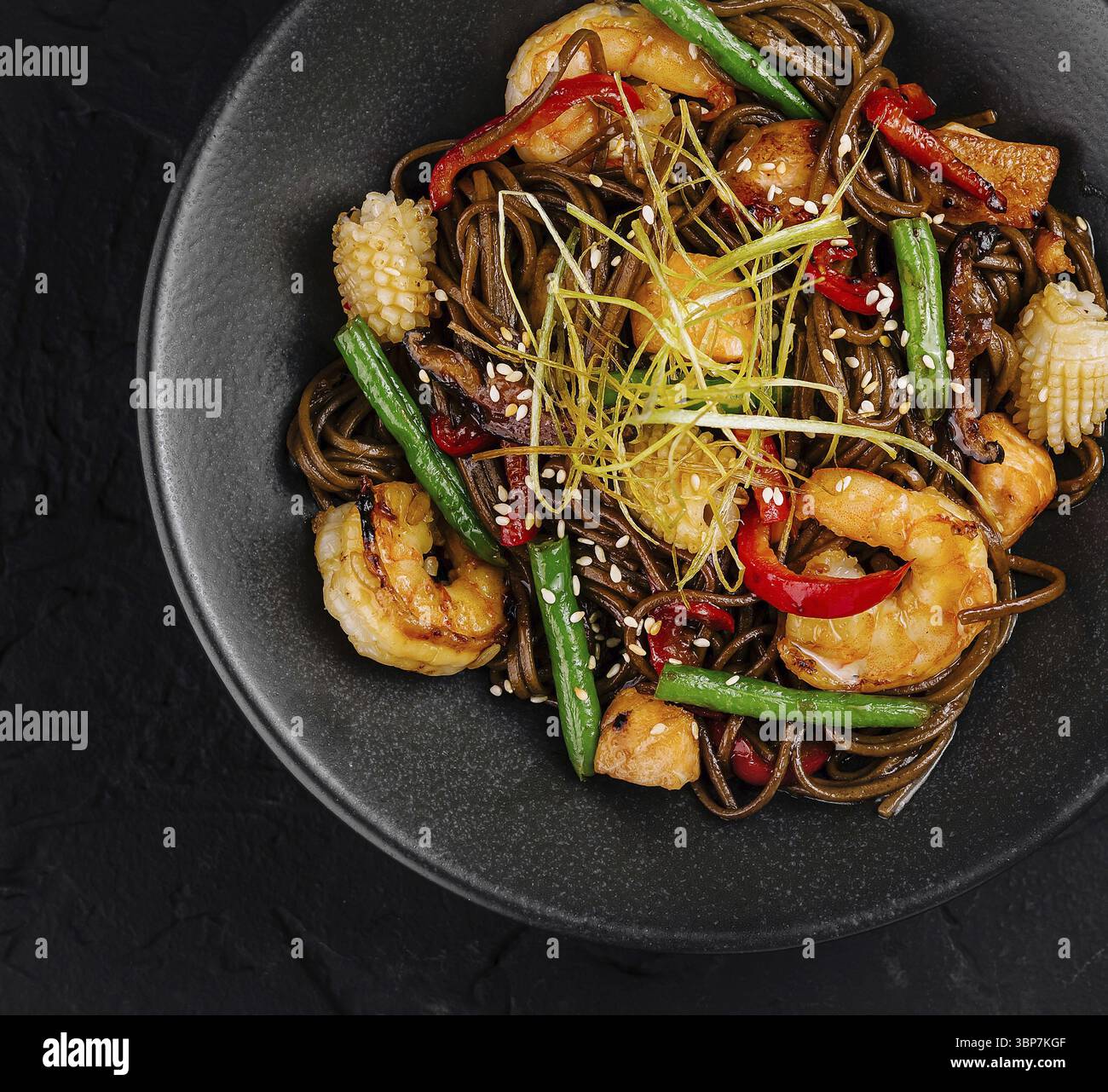 Cibo, cucina asiatica: Spaghetti saltati in padella con gamberi, verdure e guarnire in una ciotola nera su uno sfondo scuro Foto Stock