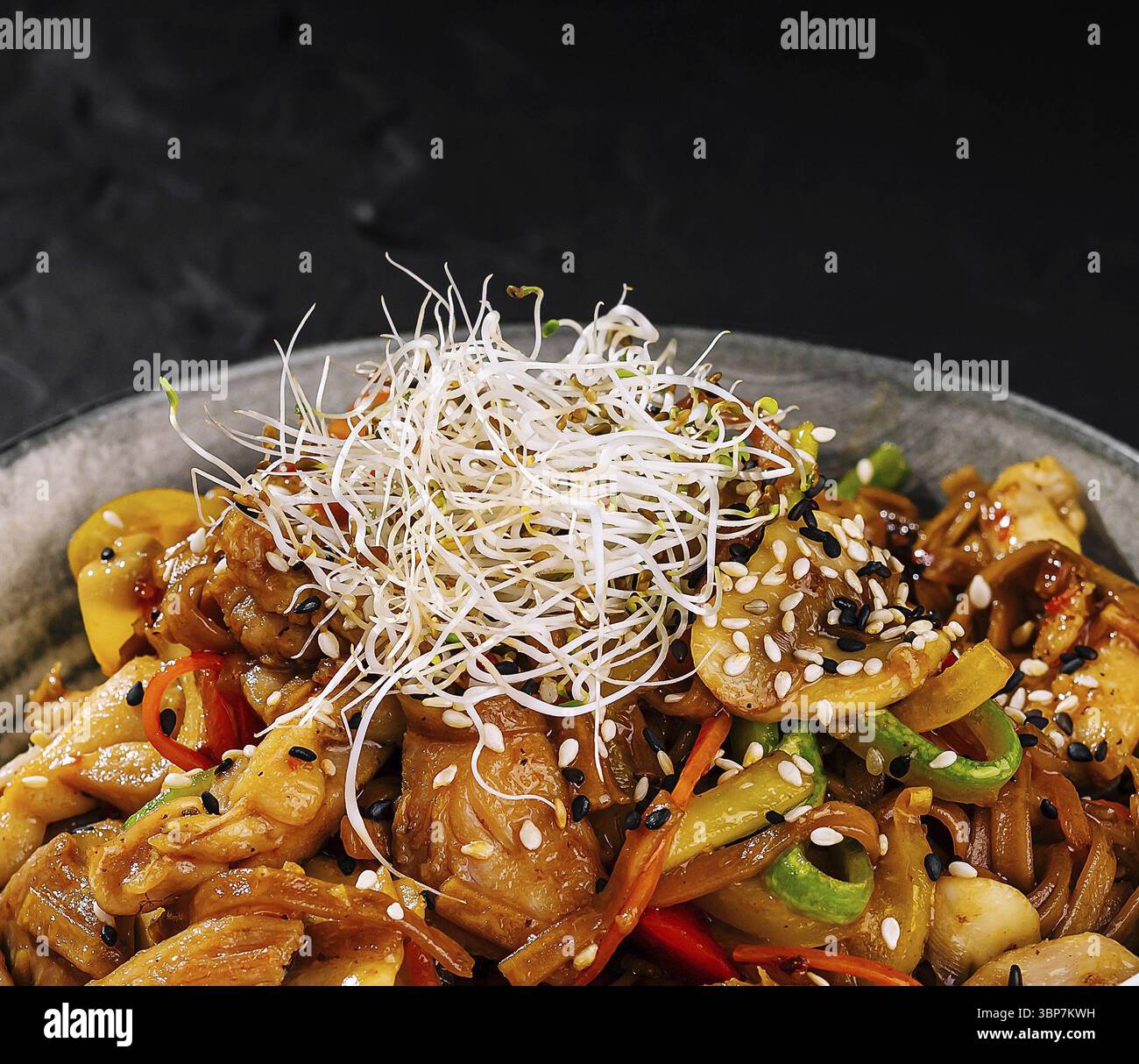 Cibo, pollo salato saltato in padella con verdure colorate e semi di sesamo su sfondo scuro Foto Stock