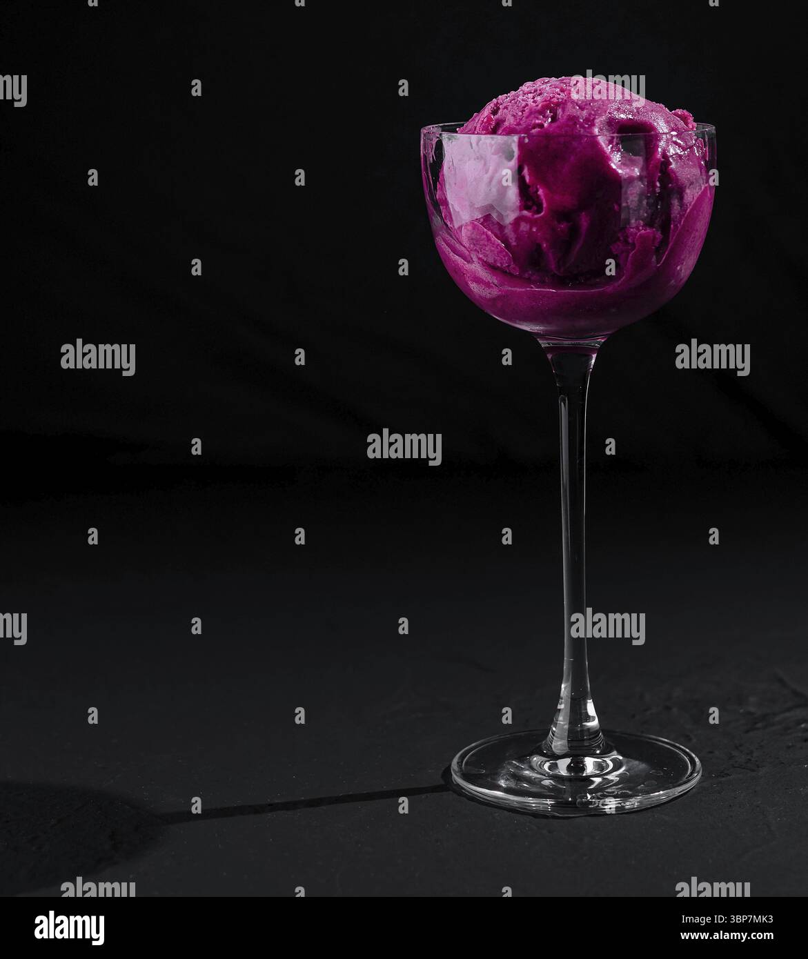 Cibo, primo piano di un invitante sorbetto di lamponi servito in un bicchiere delicato su uno sfondo scuro Foto Stock