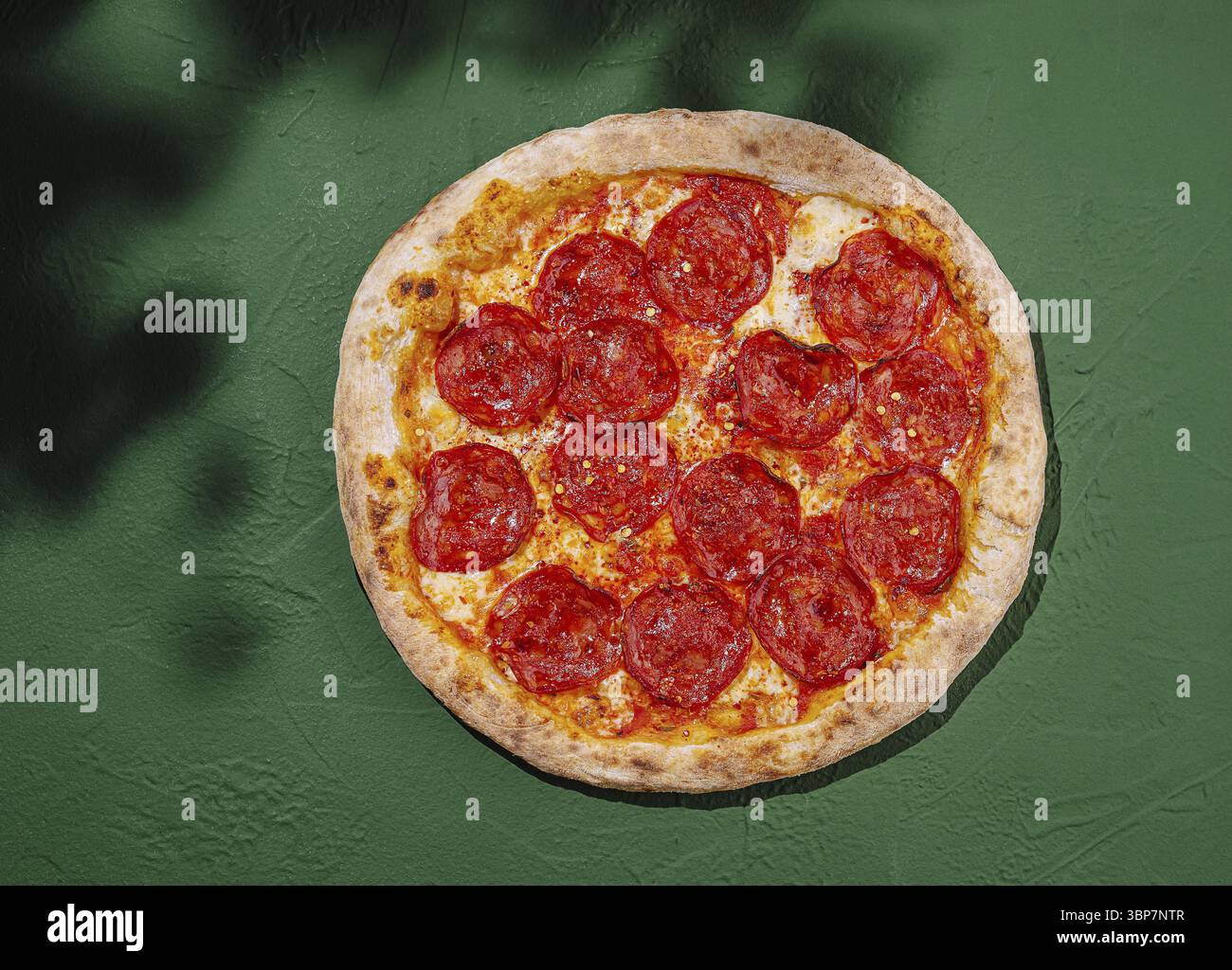 Cibo: La pizza al peperoni appena sfornata presenta crosta croccante ricoperta di formaggio fuso e fette piccanti di peperoni, che riposano su una superficie verde vivace Foto Stock