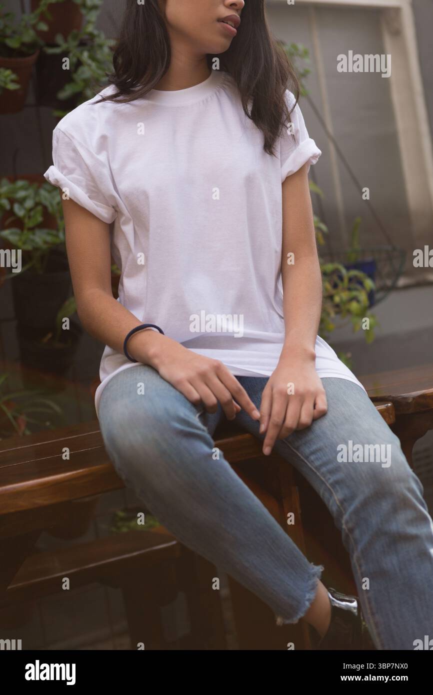 La donna è seduta su una panchina di legno nel patio esterno con piante in vaso, in un design piatto Foto Stock