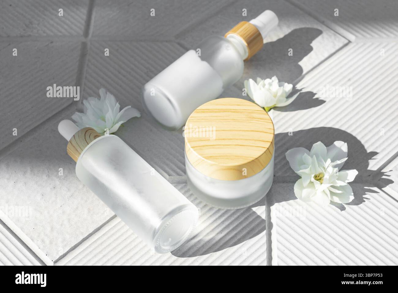 Concetto di cura della pelle. Un set di prodotti cosmetici, creme e siero. Bottiglie di vetro smerigliato su fondo di cemento grigio con ombre dure e jasmine volato Foto Stock