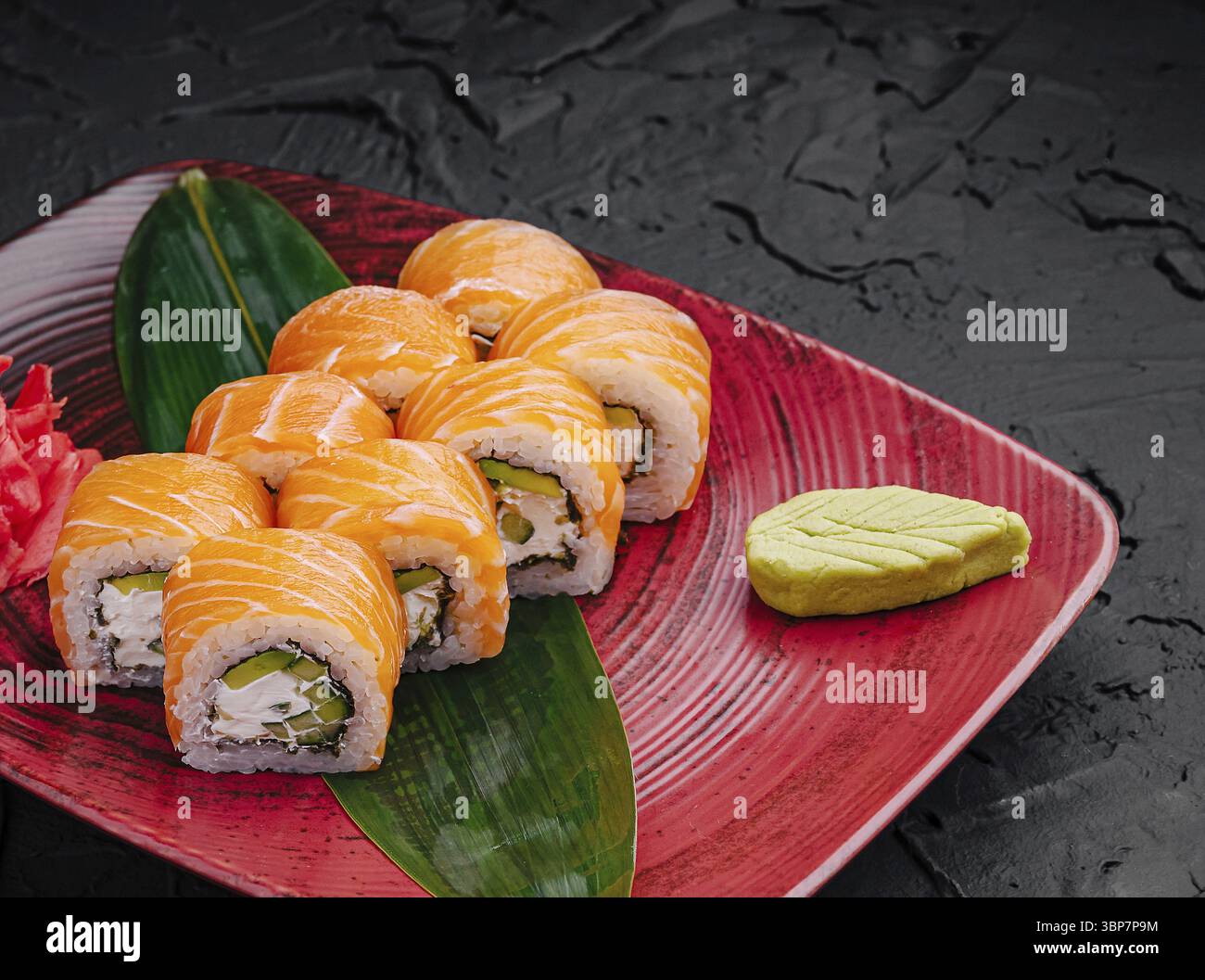 Cibo, coloratissimi sushi roll sono disposti ordinatamente su un piatto rosso vivace, accompagnati da wasabi e guarniti con zenzero sottaceto Foto Stock