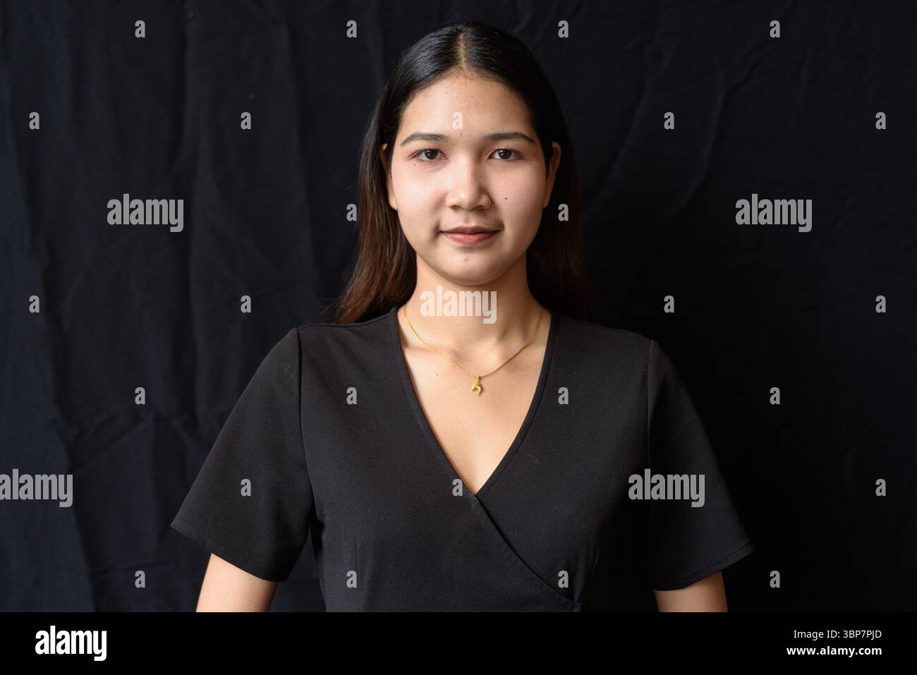 Giovane donna asiatica in abito nero che posa contro la tenda nera in luce naturale Foto Stock