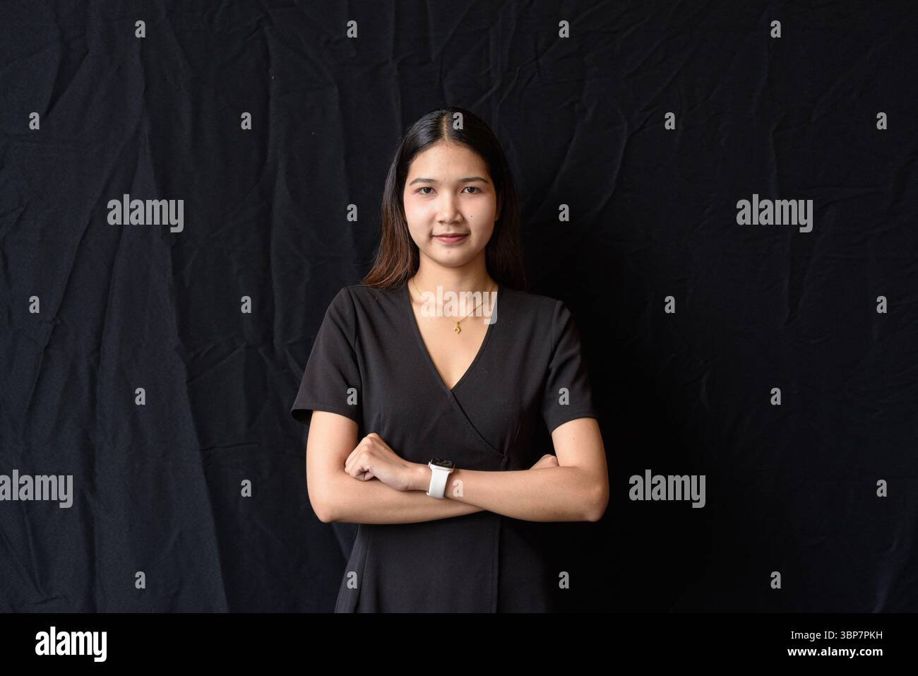 Giovane donna asiatica in abito nero che posa contro la tenda nera in luce naturale Foto Stock
