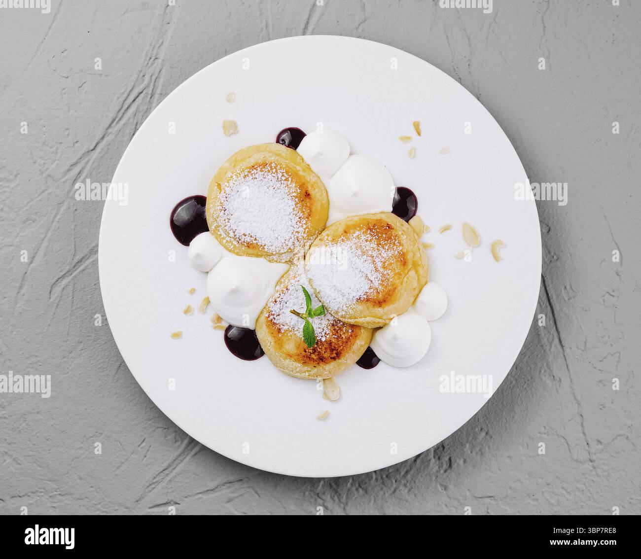 Cibo, elegante porzione di pancake conditi con zucchero a velo, panna e salsa di bacche su un piatto bianco Foto Stock