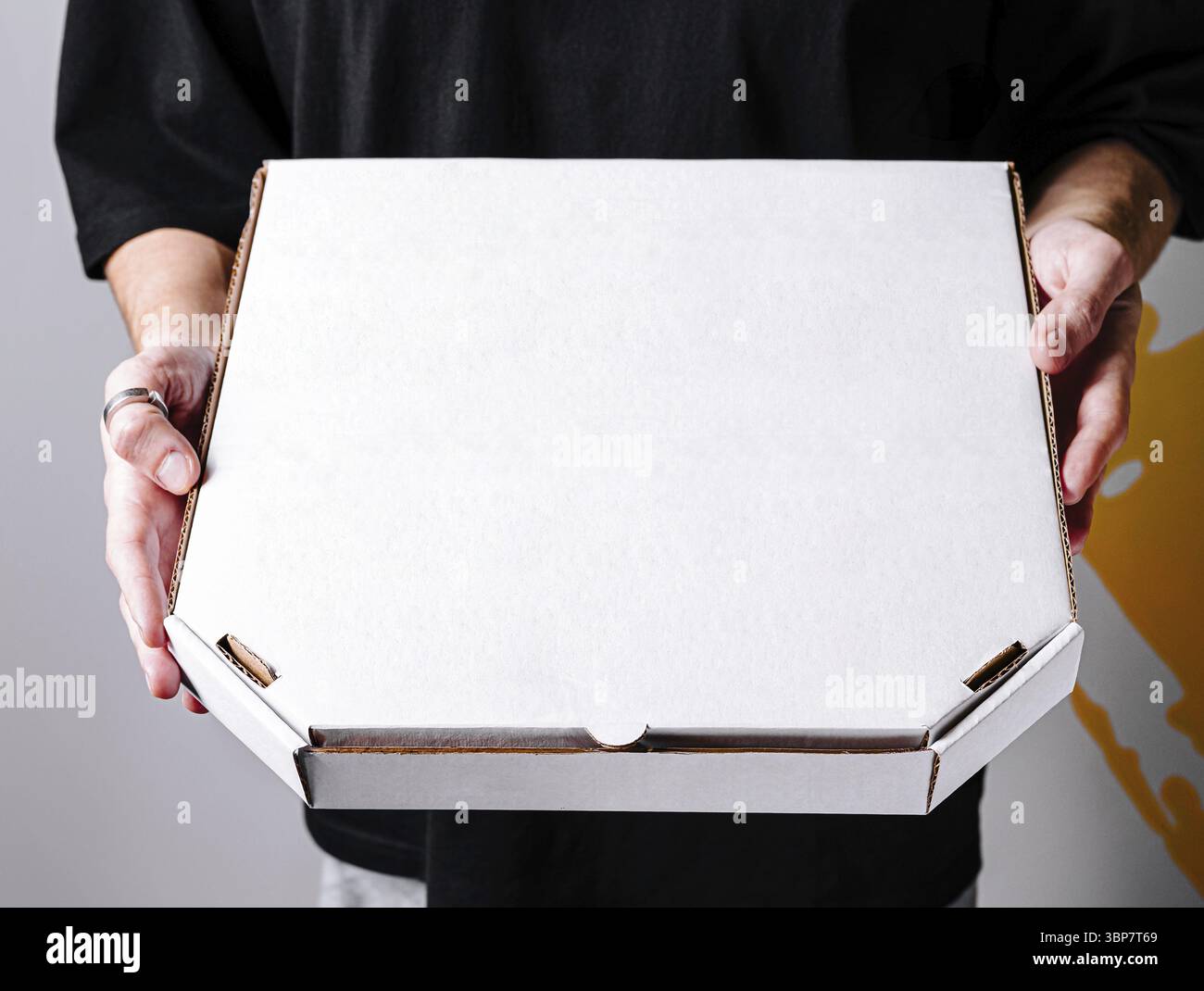 Cibo, Una persona sta in piedi con le mani tese, presentando una semplice scatola bianca per pizza. Lo sfondo presenta colori vivaci, che aggiungono emozioni a t Foto Stock