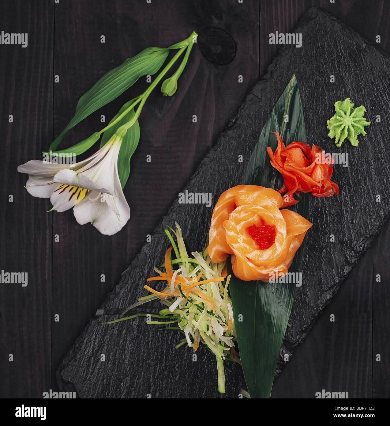 Cibo, delizioso antipasto al salmone sashimi servito su ardesia nera con wasabi, zenzero sottaceto, salsa di soia e fiore bianco Foto Stock