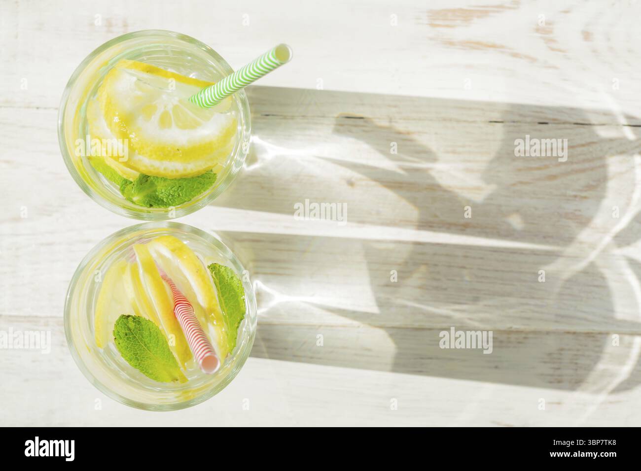 Bicchiere di limonata fatta in casa con limoni, menta e cannucce di carta su fondo rustico in legno. Bevanda rinfrescante estiva. ombre dure Foto Stock